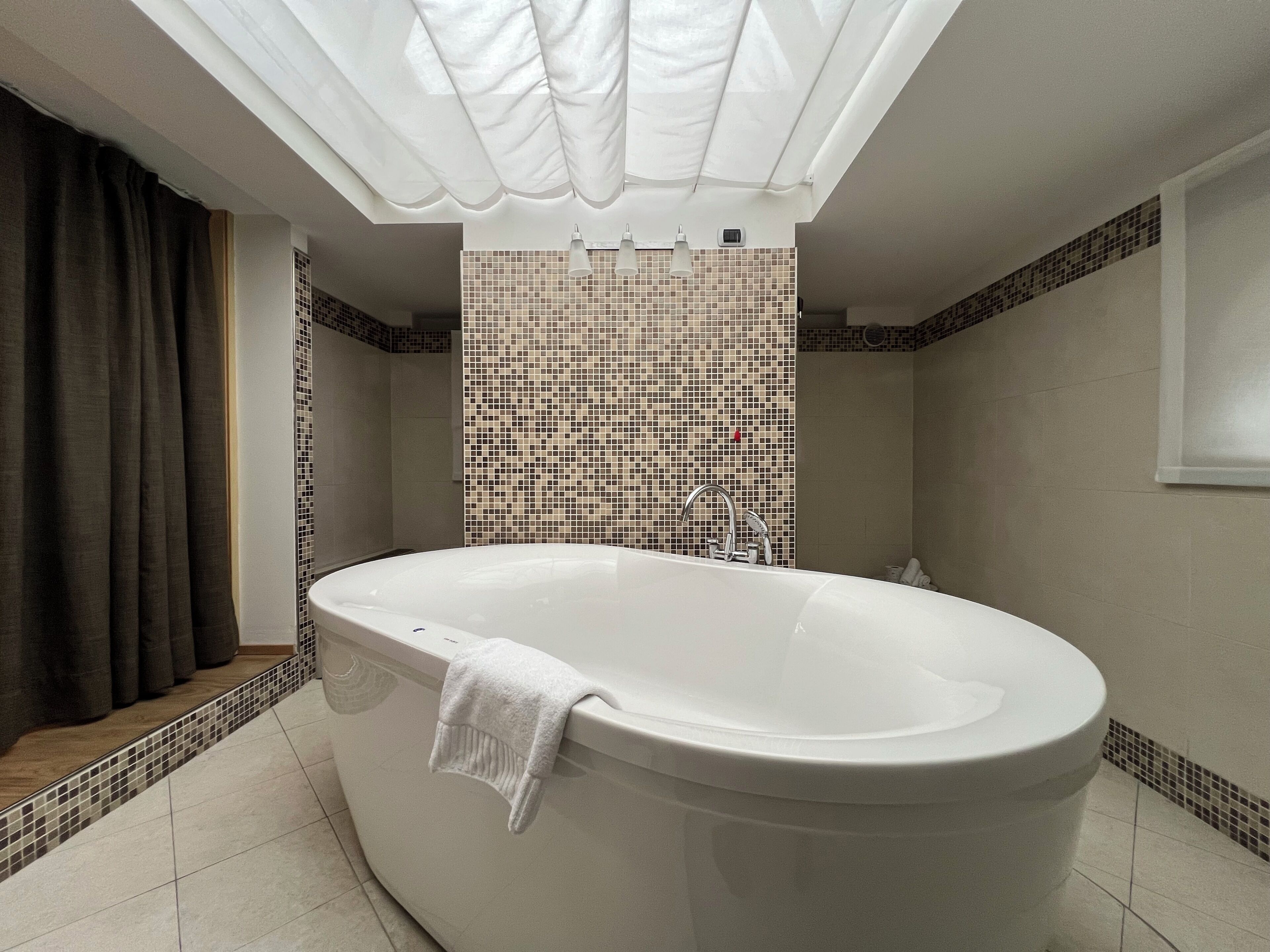 A modern bathroom with a freestanding bathtub, a shower area, and a tiled wall with a mosaic pattern.