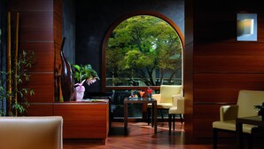 Un interior moderno con mostrador de recepción, zona de estar y ventanas amplias que ofrecen vistas a árboles.