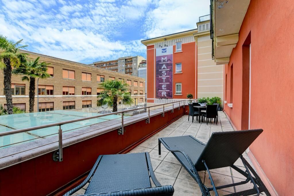 Un área de piscina en la azotea con sillones, baranda de cristal y un edificio con un letrero que dice 'MASTER'.