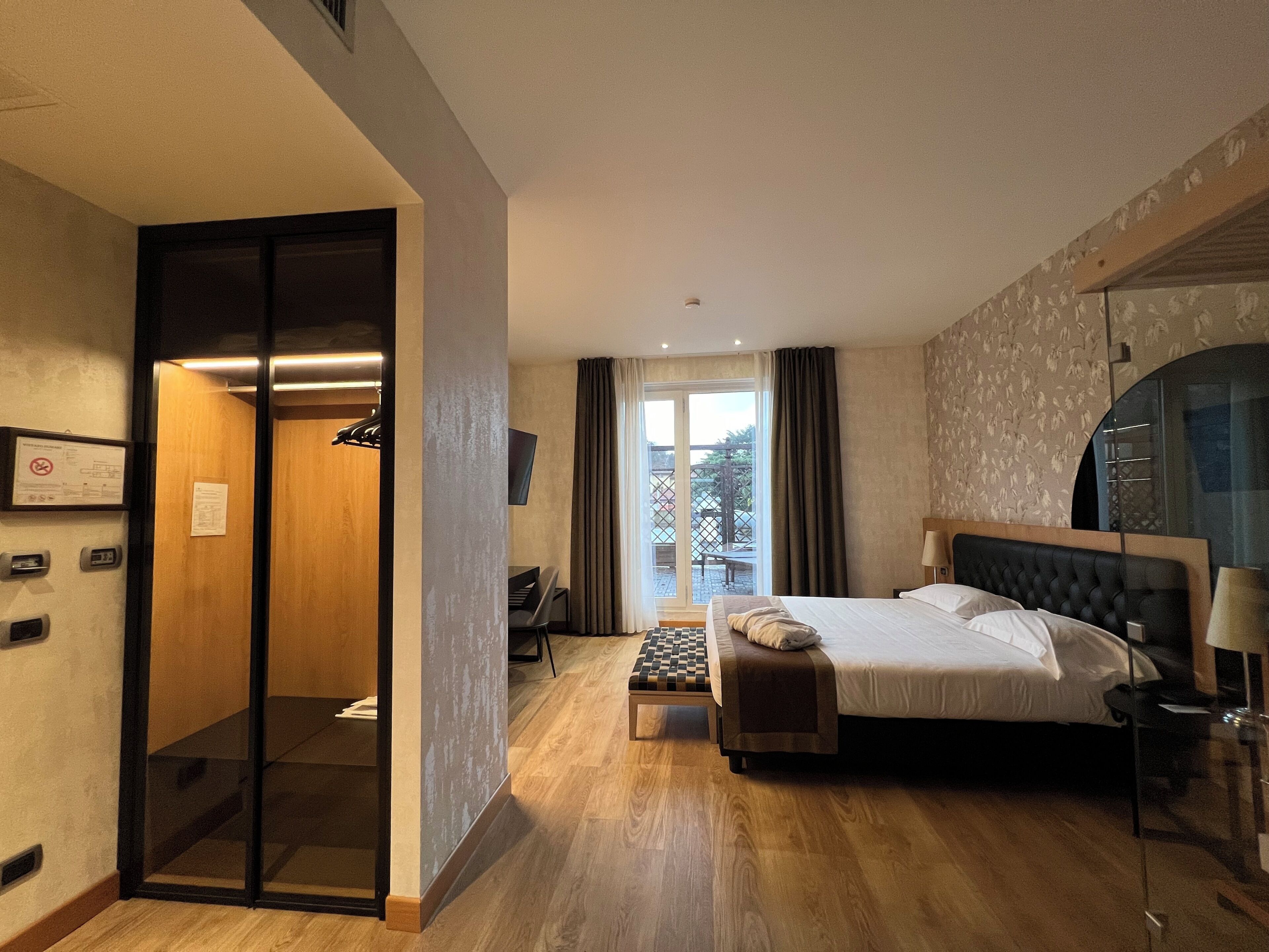 A hotel room with a bed, a desk, a chair, a television, and a sliding door to a balcony.