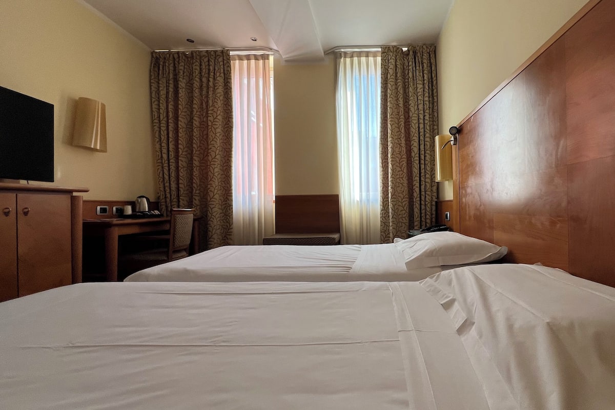A hotel room with two beds, a desk with a telephone, a chair, and a television on the wall.