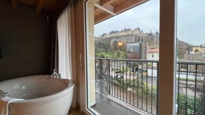 Un baño con bañera y balcón con vista a un castillo y al paisaje urbano.