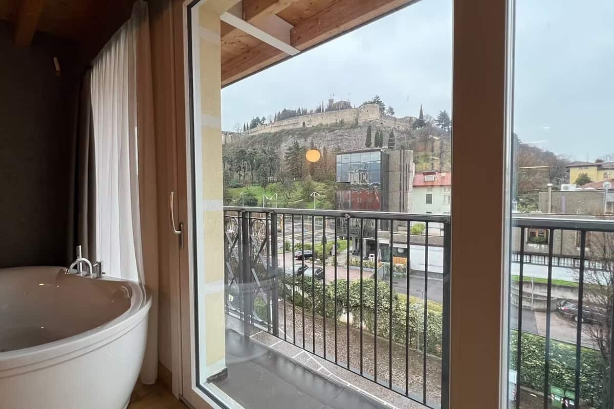 A bathroom with a bathtub and a balcony with a view of a castle and cityscape.