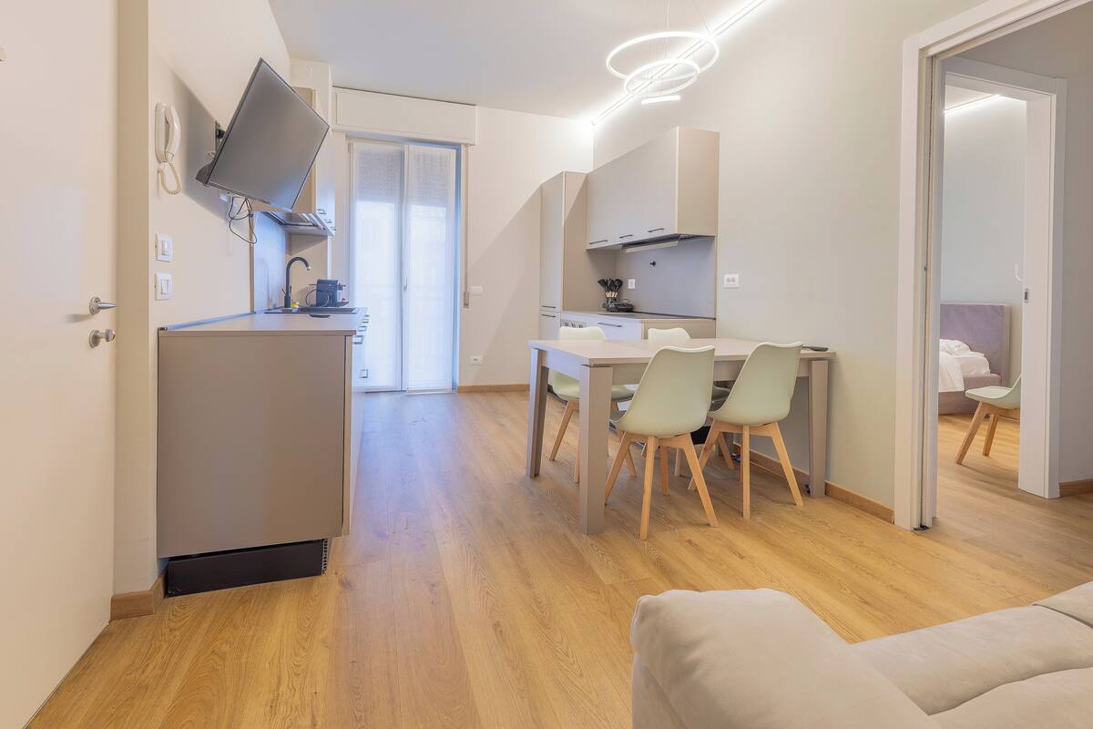 A modern hotel room with a dining area, a kitchenette, and a separate bedroom.