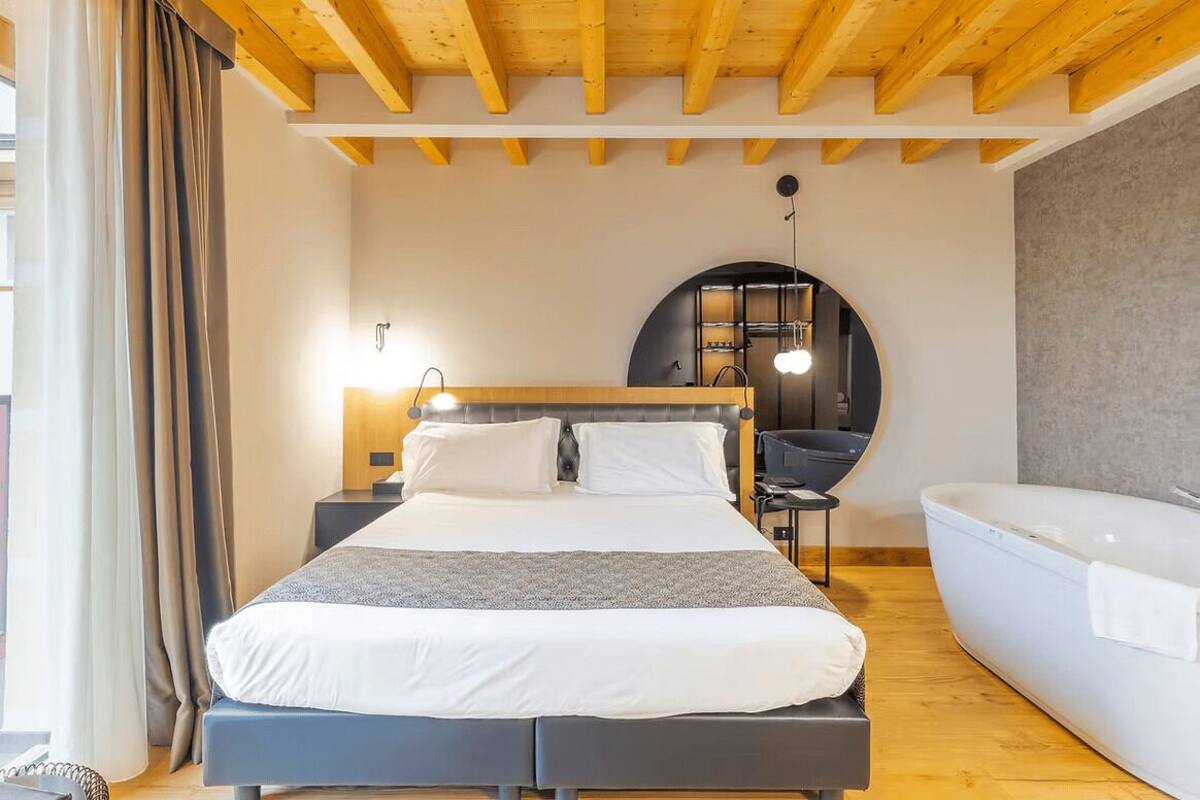 A bedroom with a bed, a desk, a chair, a round mirror, and a bathtub.