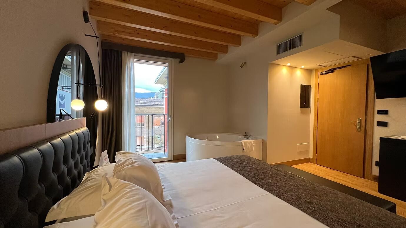 Habitación de hotel con cama, bañera, puerta de madera y vista por la ventana.