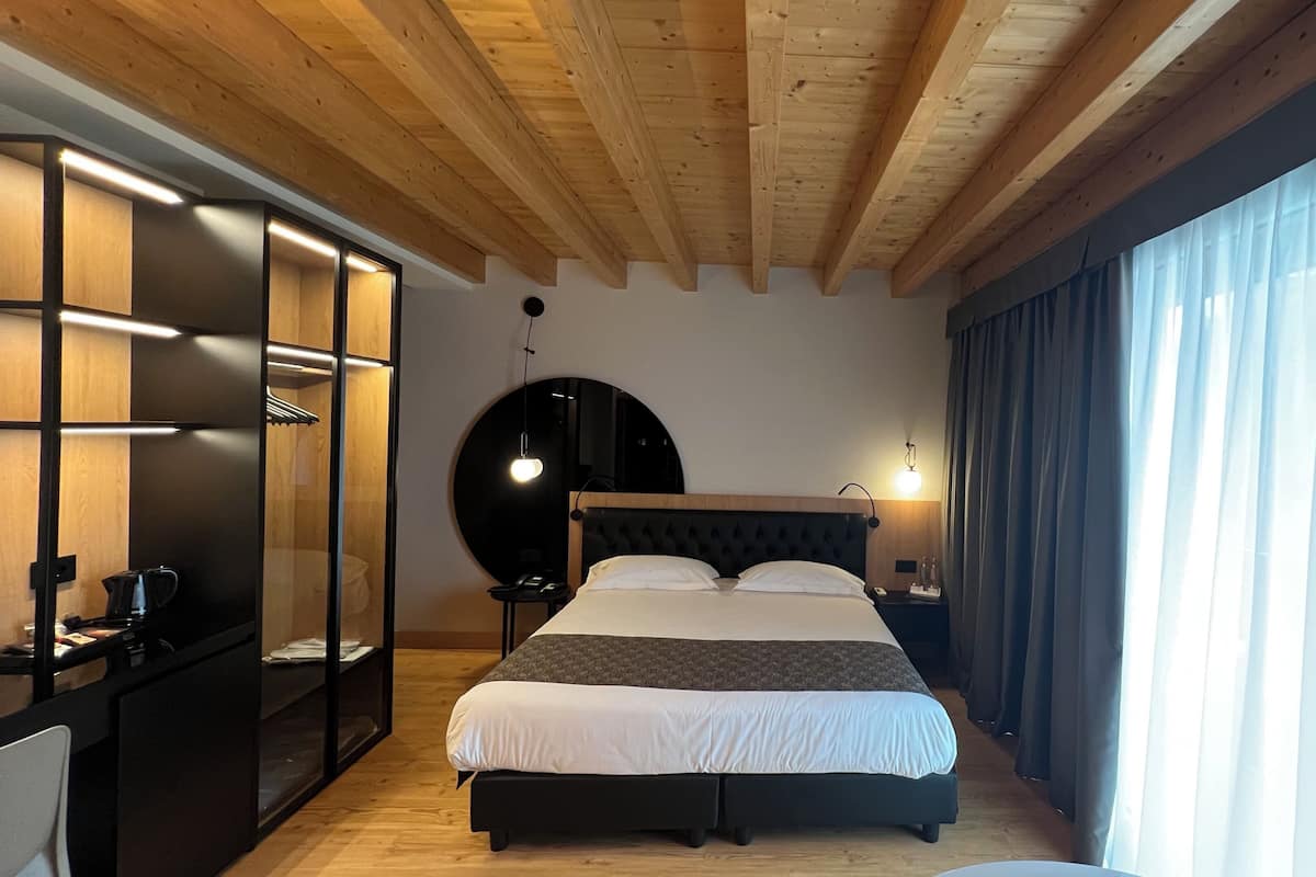 A bedroom with a bed, a round mirror, a nightstand, and a window with curtains.