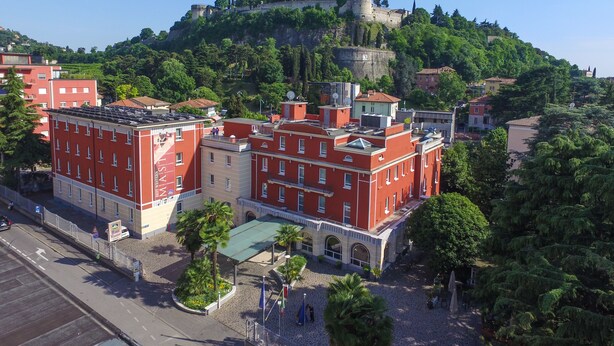 Un hotel de fachada roja, situado en una ciudad con un castillo histórico en una colina.