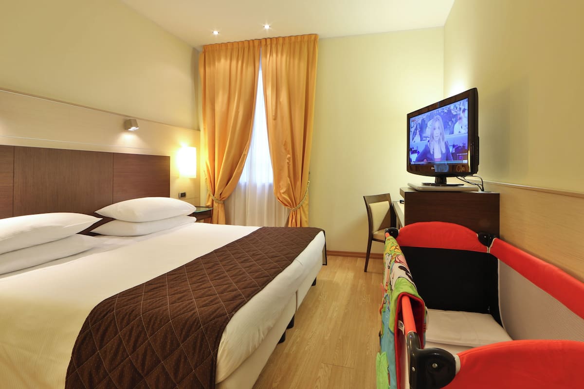 A hotel room with a bed, a television, a desk, and a chair.