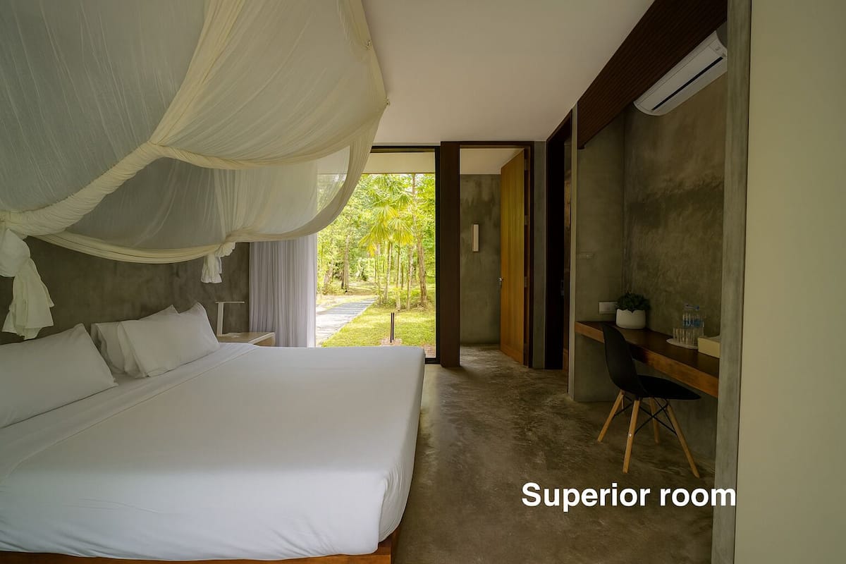 A superior room with a large bed, a desk, and a view of a garden.