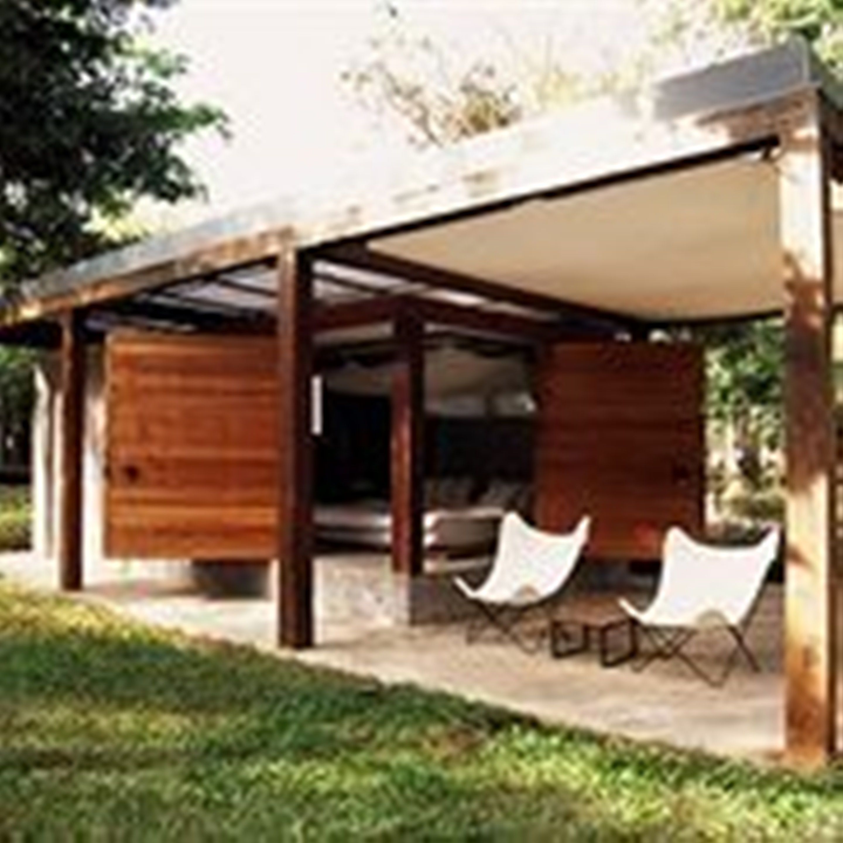 Una estructura moderna al aire libre con fachada de madera, un área de descanso cubierta y una vista despejada del entorno verde.