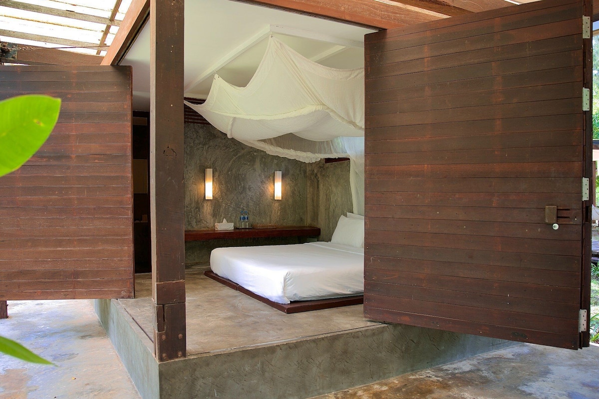 A room with a bed, a nightstand, and a wall-mounted light fixture.