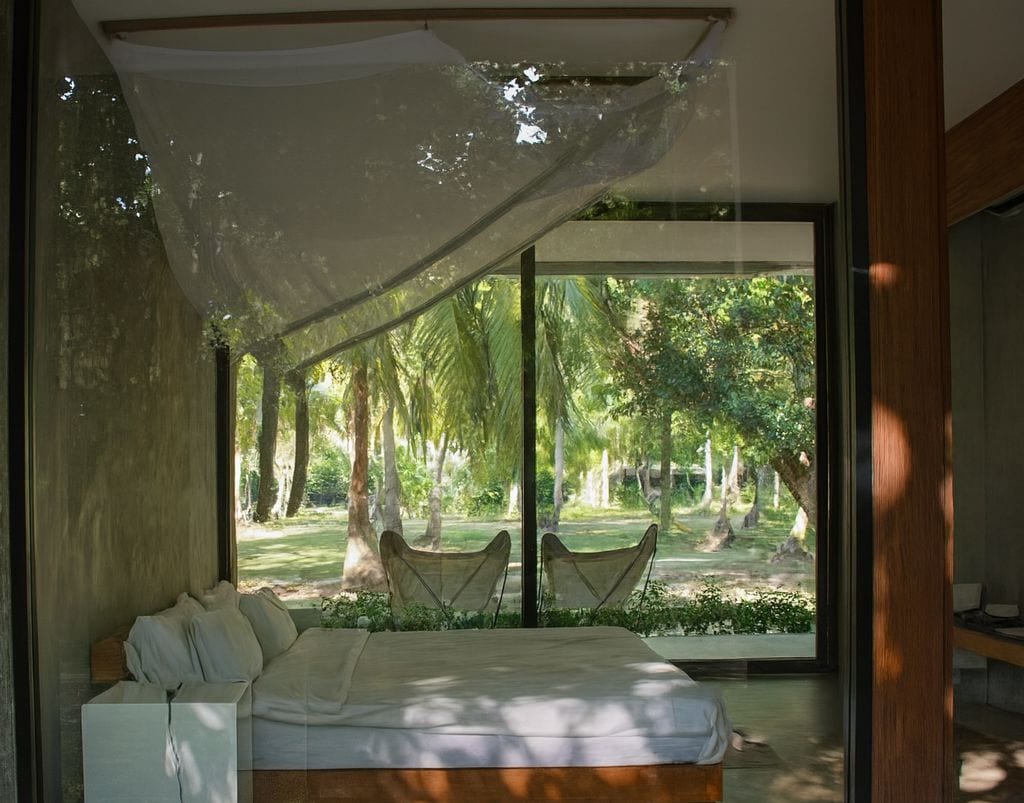 Una habitación superior con una cama grande, vistas de un jardín a través de puertas de cristal y un dosel sobre la cama.