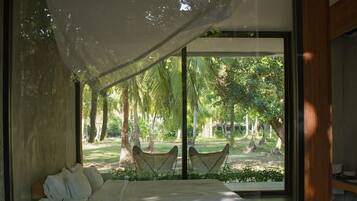 Una habitación superior con una cama grande, vistas de un jardín a través de puertas de cristal y un dosel sobre la cama.