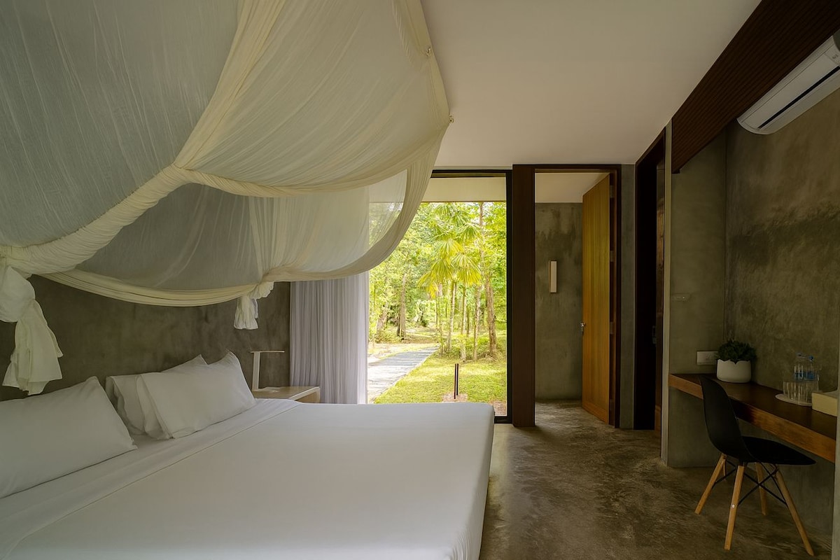 A superior room with a large bed, a desk, and a view of a garden.