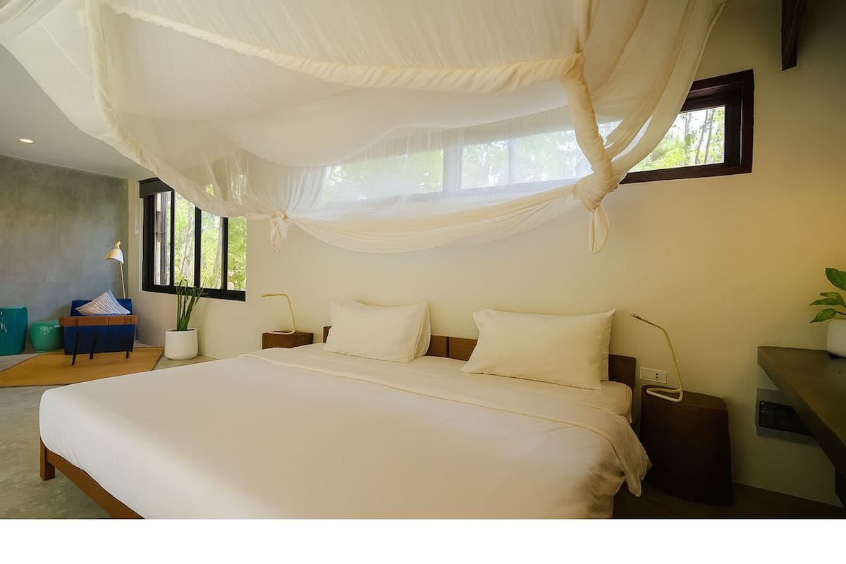 A bedroom with a large bed, bedside tables, a nightstand, a window, and a potted plant.