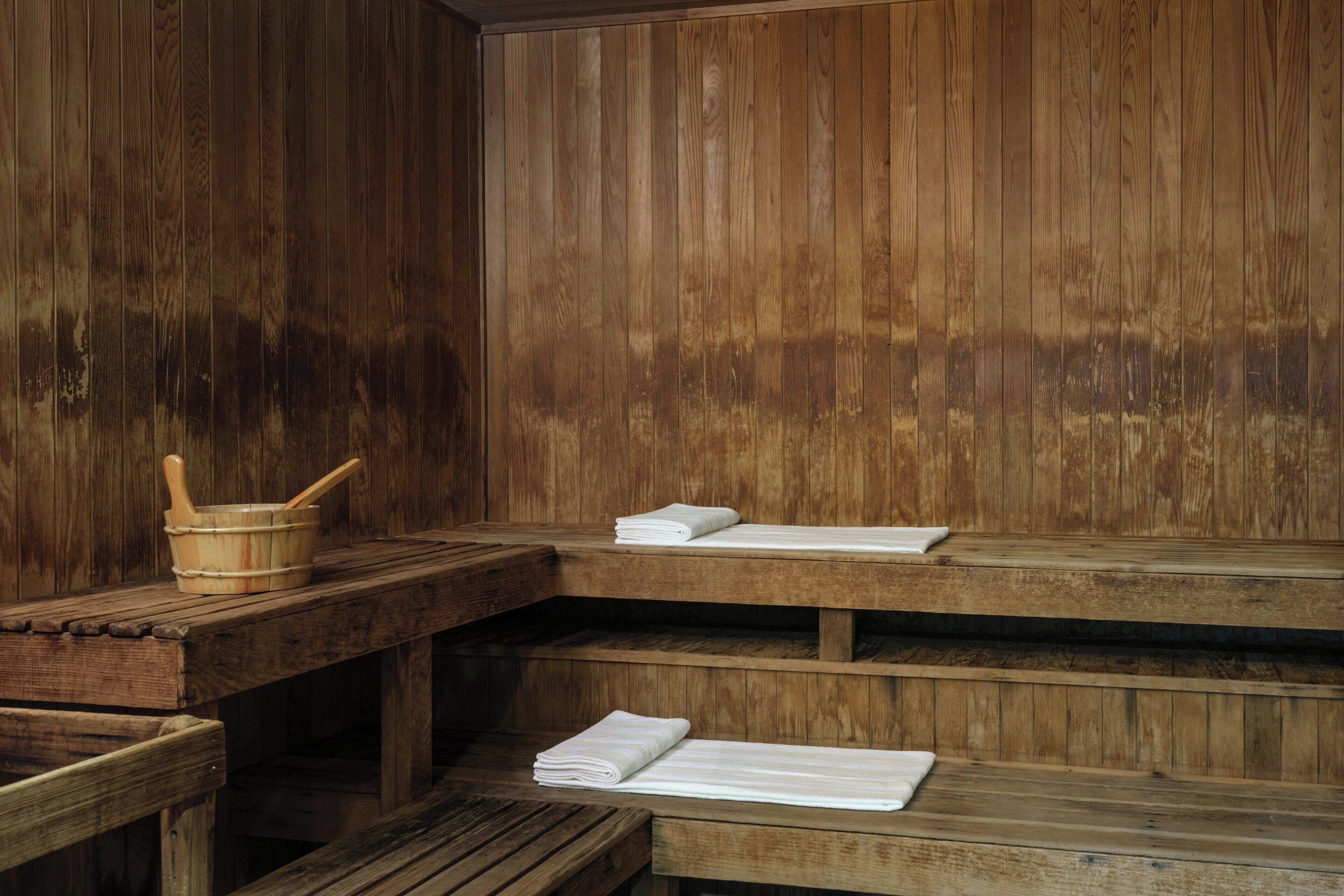 A wooden sauna with benches and a wooden table with towels and a wooden bowl.