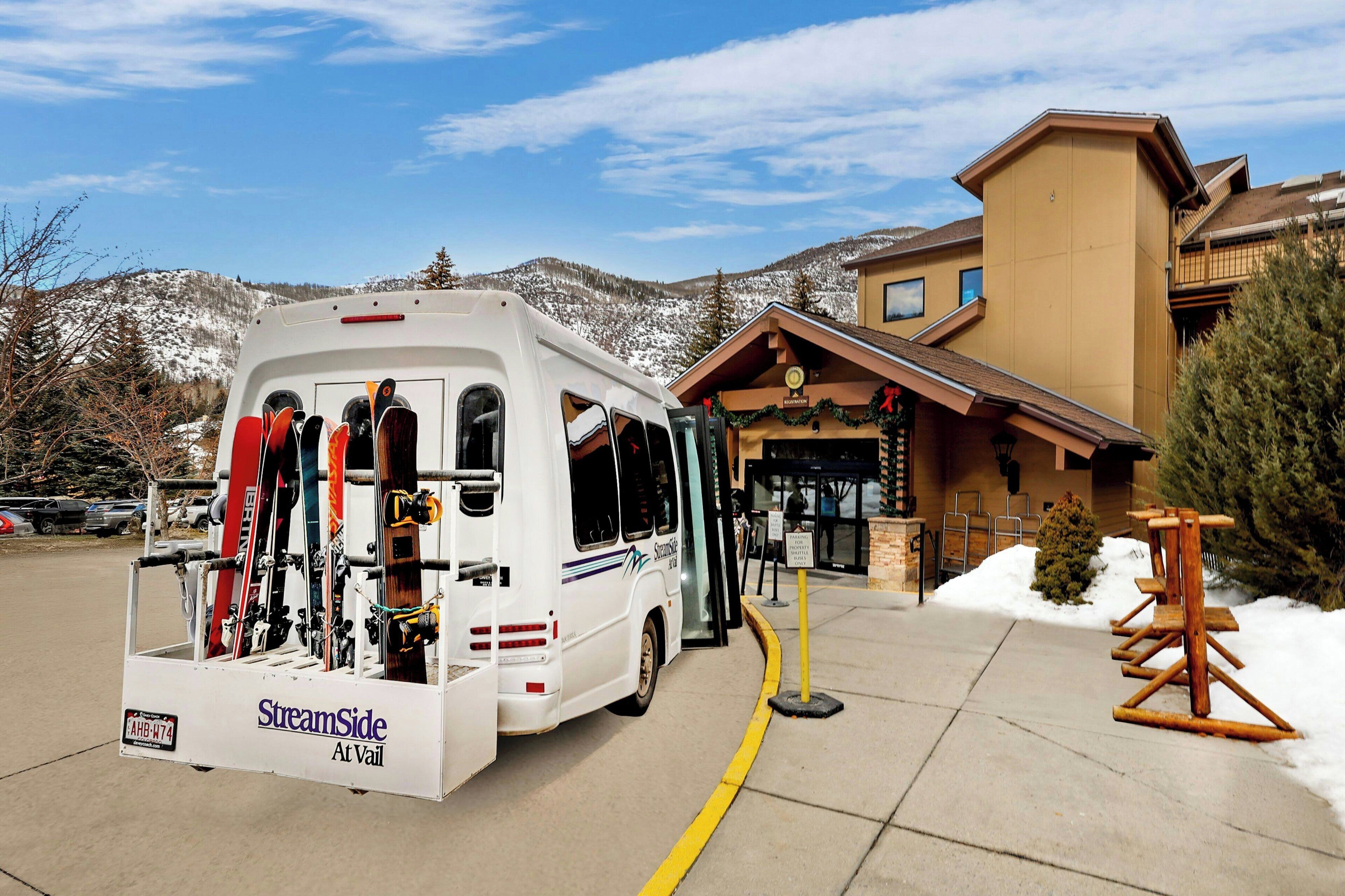 A white RV with skis parked in front of a building with a wooden facade and a sign that reads "StreamSide At Vail."