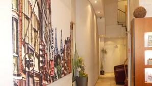 Ein Flur mit großformatiger Stadtansicht-Mural, einer Topfpflanze und einer Treppe, die in ein Obergeschoss führt.