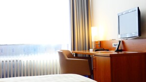 Ein Hotelzimmer mit einem Bett, einem Schreibtisch mit Lampe, einem Fernseher und einem Sessel.