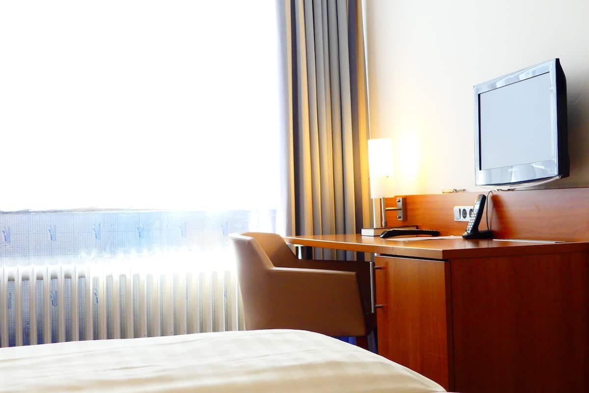 A hotel room with a bed, a desk with a lamp, a television, and a chair.