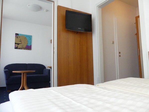 A hotel room with a bed, a TV mounted on a wooden panel, a blue sofa, and a small table.