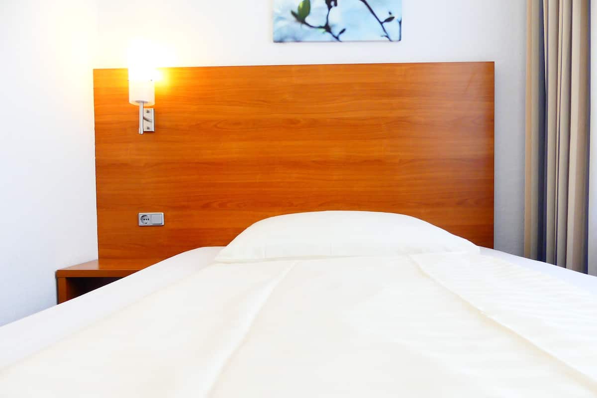 A neatly made bed with a wooden headboard, a wall-mounted light, and a power outlet.