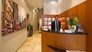 Ein Hotel-Empfangsbereich mit Rezeptionistin, einem Holzbüro, einem Blumentopf und einer Wand mit gerahmten Bildern.