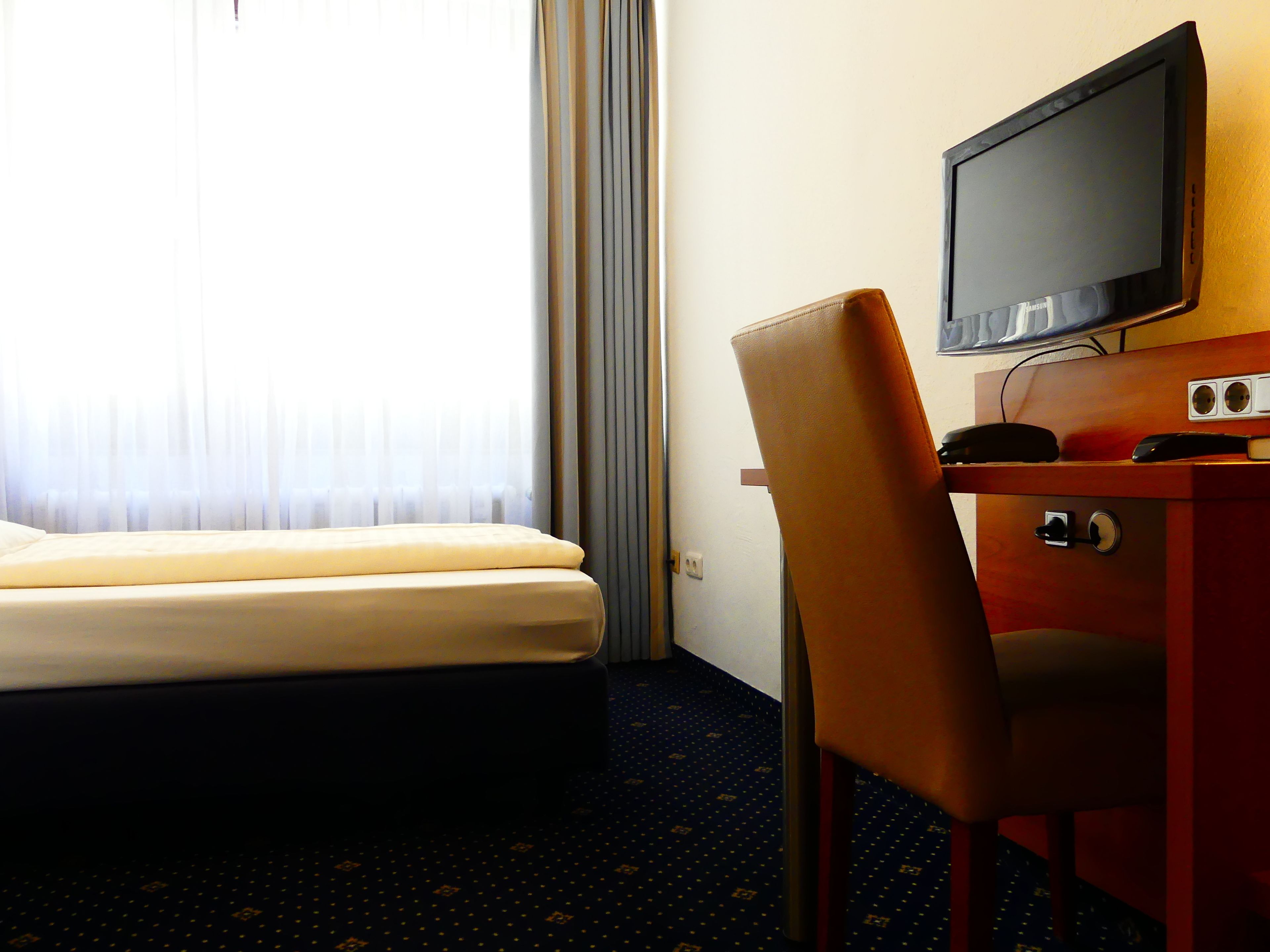 A hotel room with a bed, a desk with a television, and a chair.