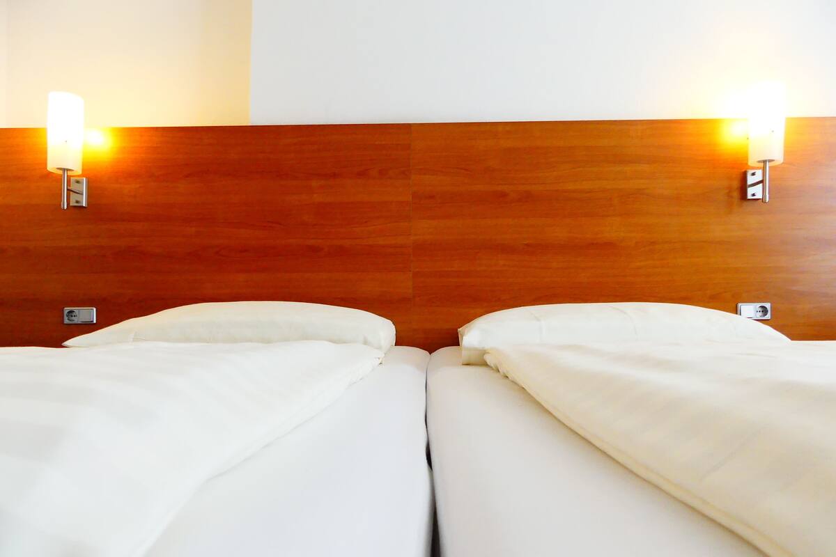 A hotel room with two single beds, wooden headboard, and wall-mounted lights.