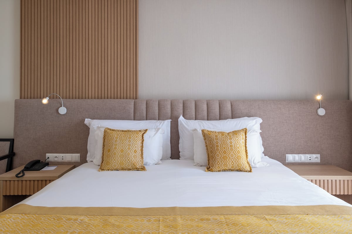 A hotel room with a large bed, two bedside tables, a telephone, and a wall-mounted light fixture.