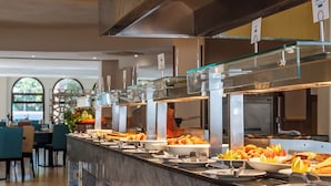 Zona de bufé con mostrador de mármol, diversos alimentos y relojes digitales que muestran la hora.