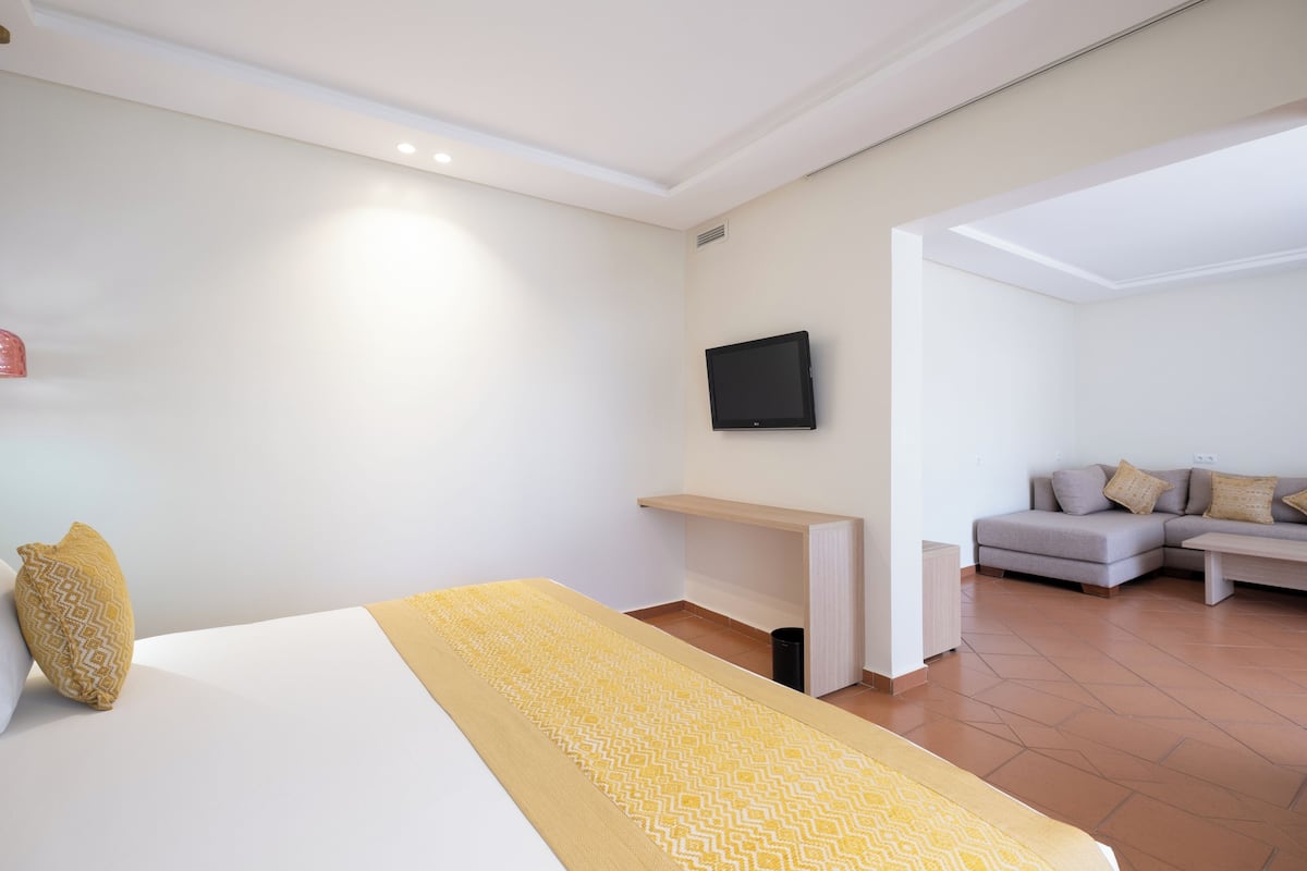 A hotel room with a bed, a TV mounted on the wall, a sofa, and a small table.