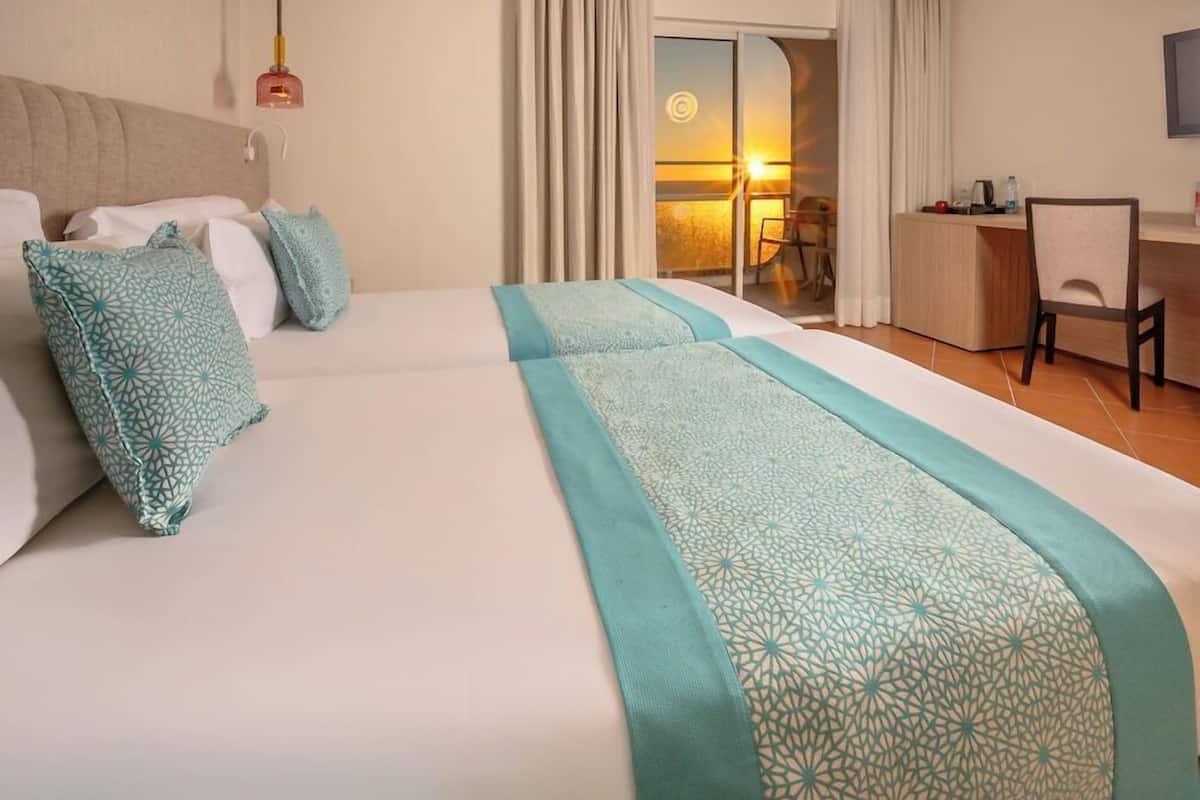 A hotel room with a bed, a desk, and a view of the sunset.