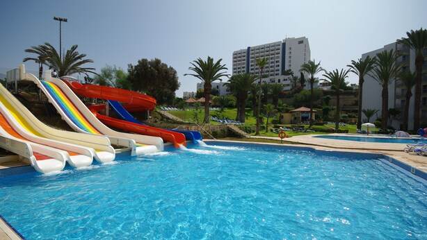 Una piscina con varias toboganes, palmeras y un edificio al fondo.