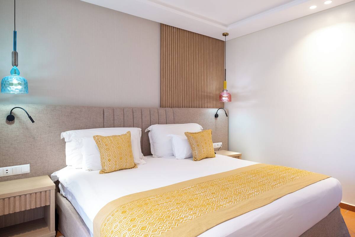 A hotel room with a large bed, a wooden headboard, a bedside table, and a wall-mounted lamp.