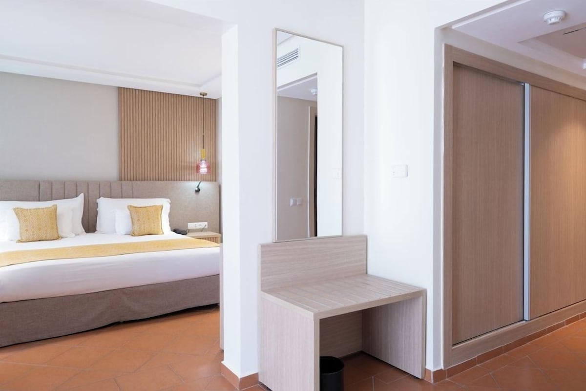 Una habitación de hotel con una cama, una mesita de noche, un espejo y un armario.