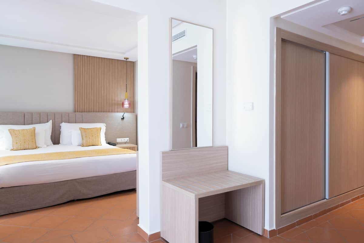 A modern hotel room with a bed, bedside table, mirror, wardrobe, and a small trash bin.