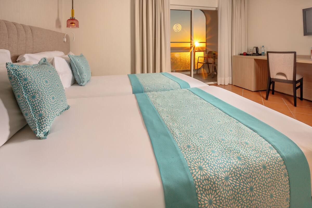 A hotel room with a large bed, a desk, and a view of the sunset.