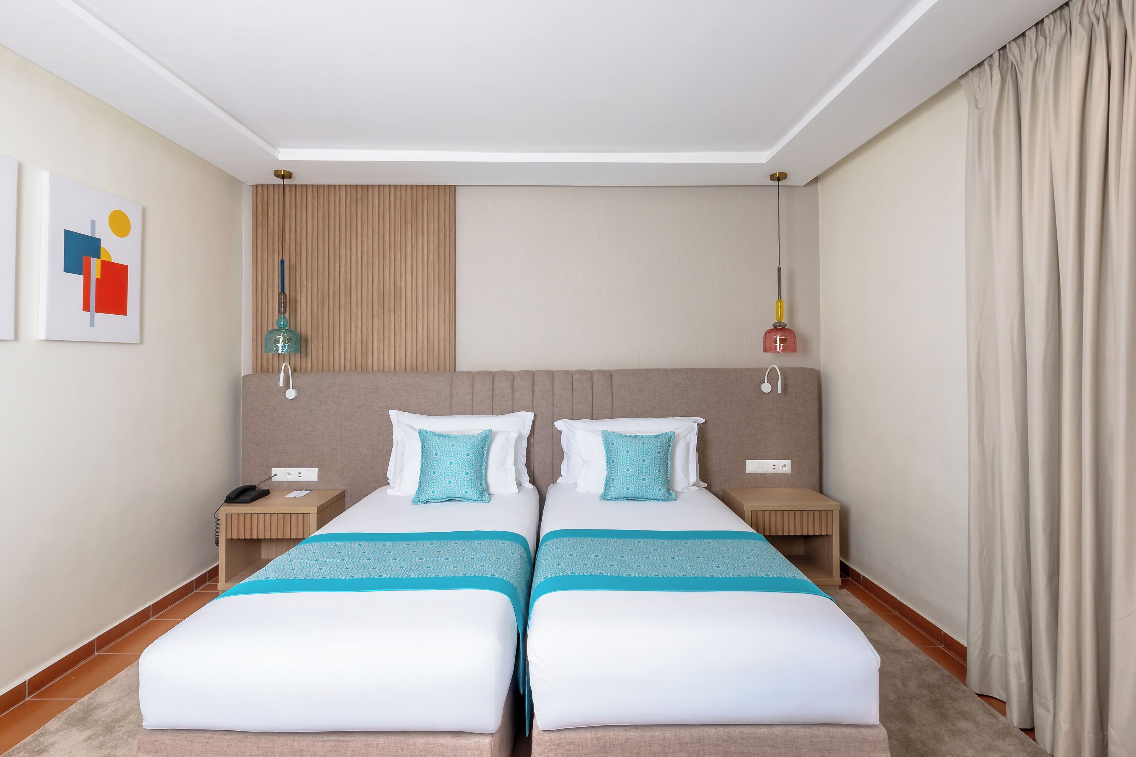 Habitación de hotel con dos camas, una mesita de noche de madera, un escritorio y una lámpara fijada a la pared.