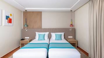 Habitación de hotel con dos camas, una mesita de noche de madera, un escritorio y una lámpara fijada a la pared.