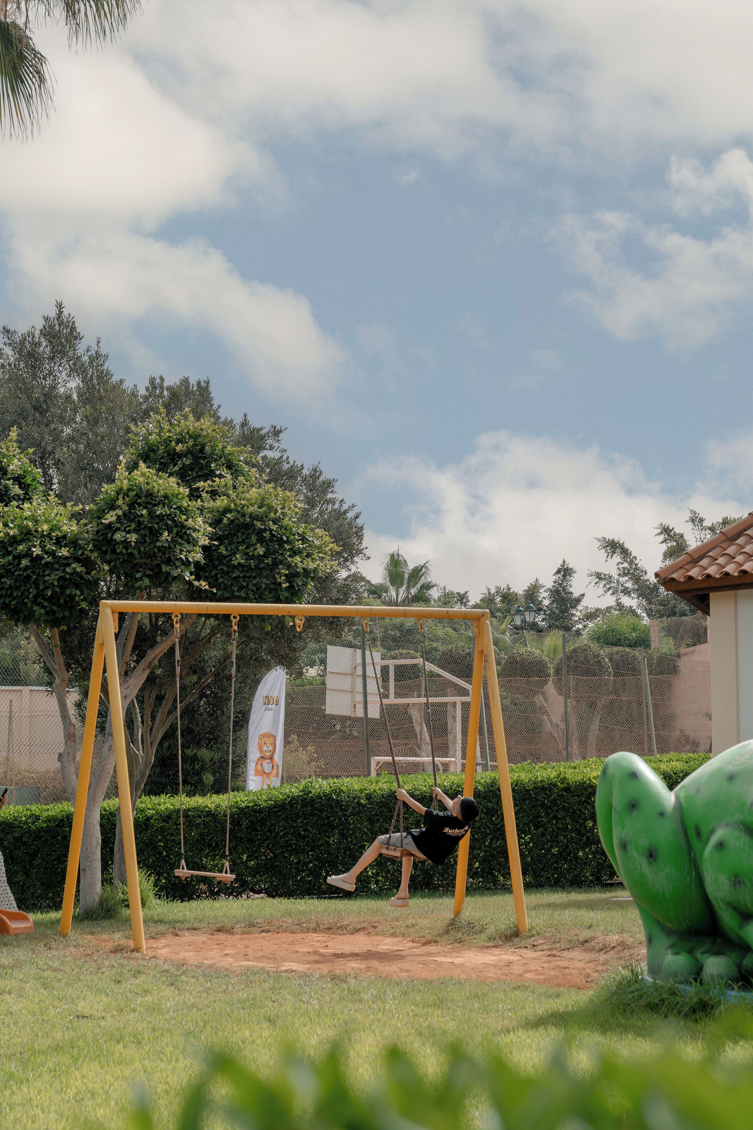 A playground with a swing set and a green sculpture.
