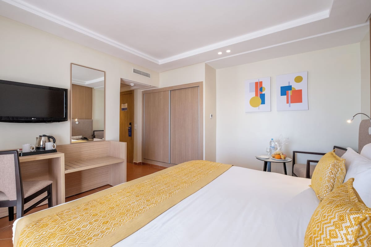 A hotel room with a bed, a desk, a TV, a wardrobe, and artwork on the wall.