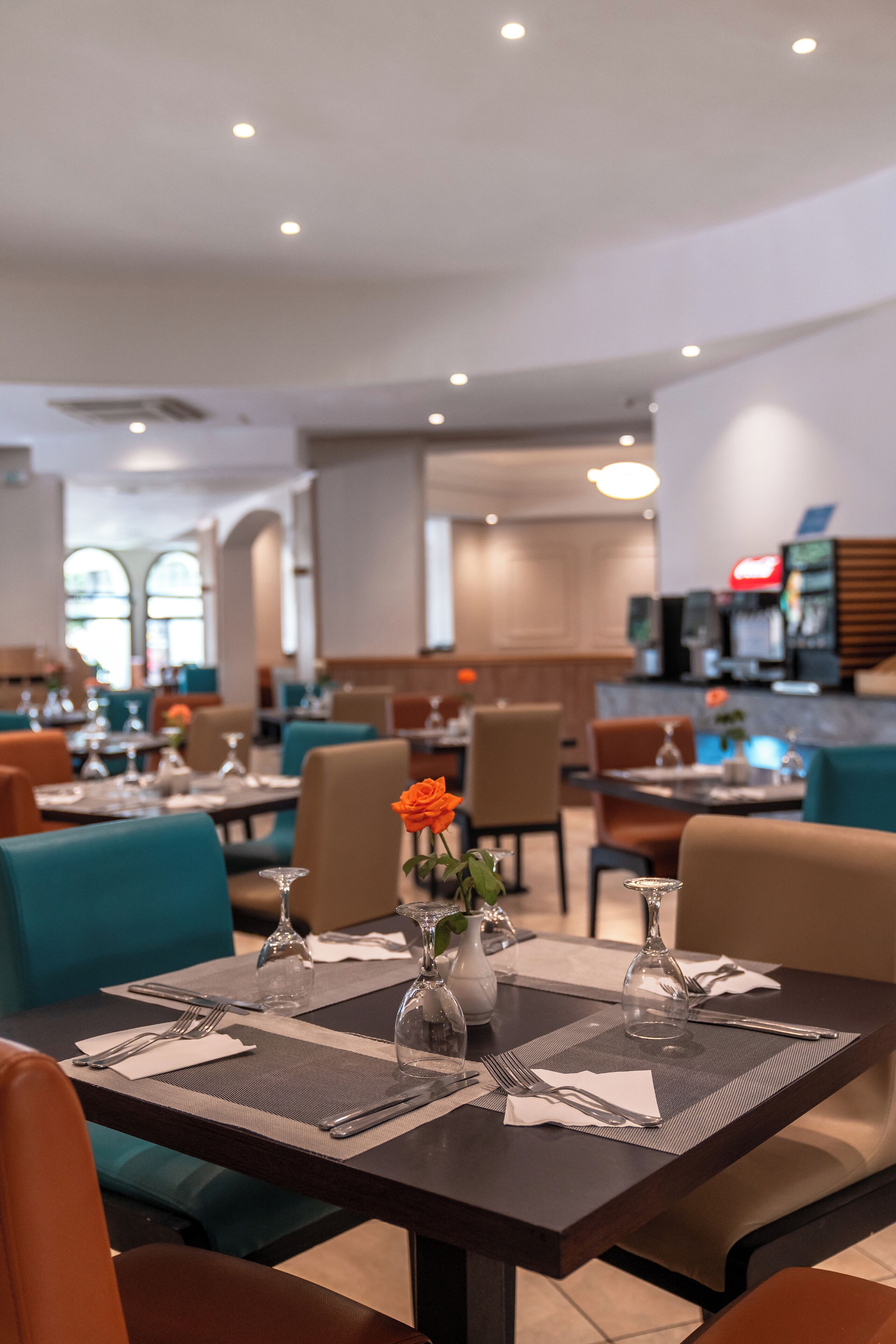 Een restaurant met gedekte tafels, oranje stoelen en een bloemstuk in een vaas.