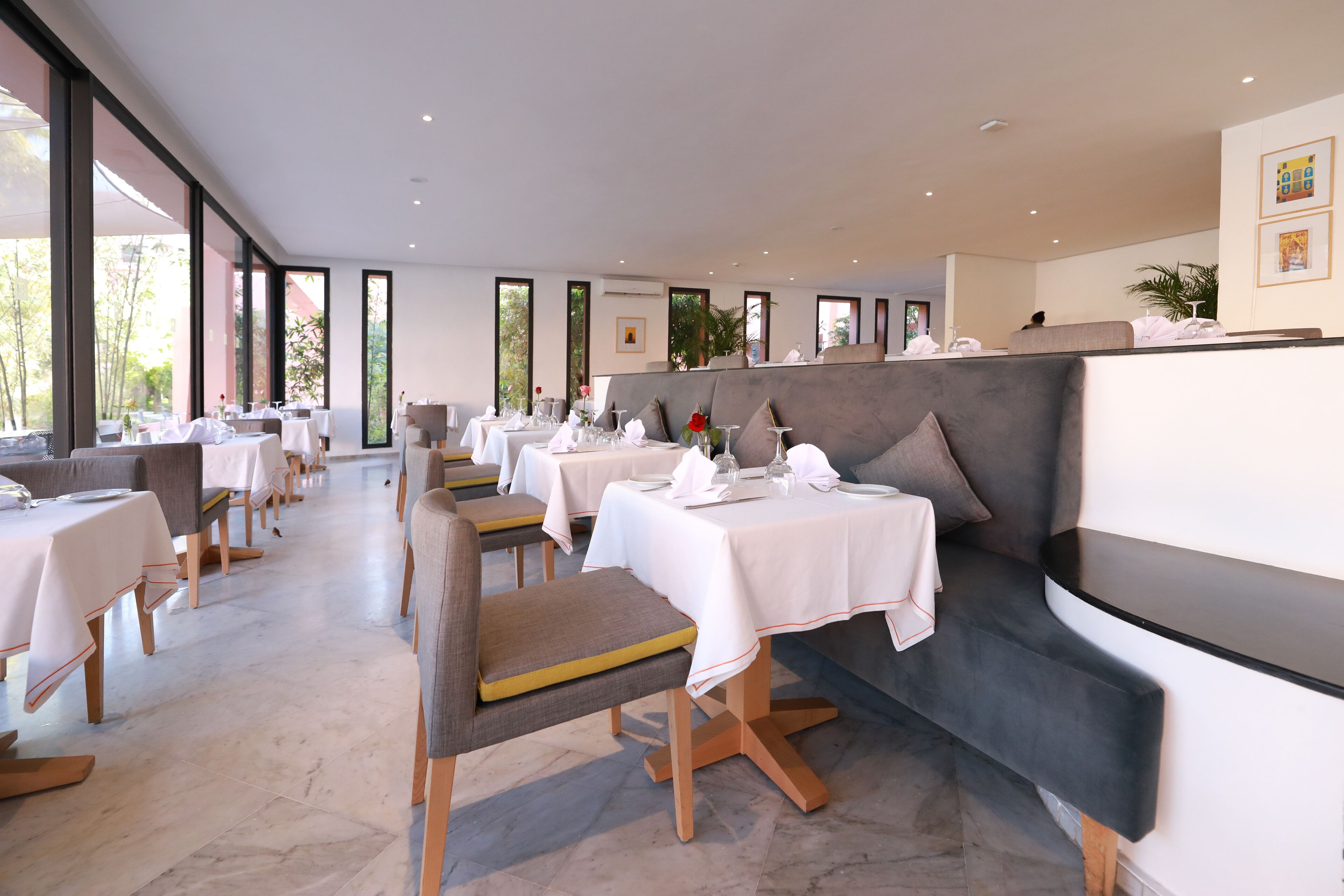 Un comedor moderno con mesas y sillas, ventanas amplias y una zona de estar con un banco gris.