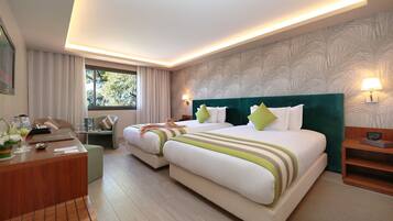 Habitación de hotel con dos camas, un escritorio y una ventana con cortinas.