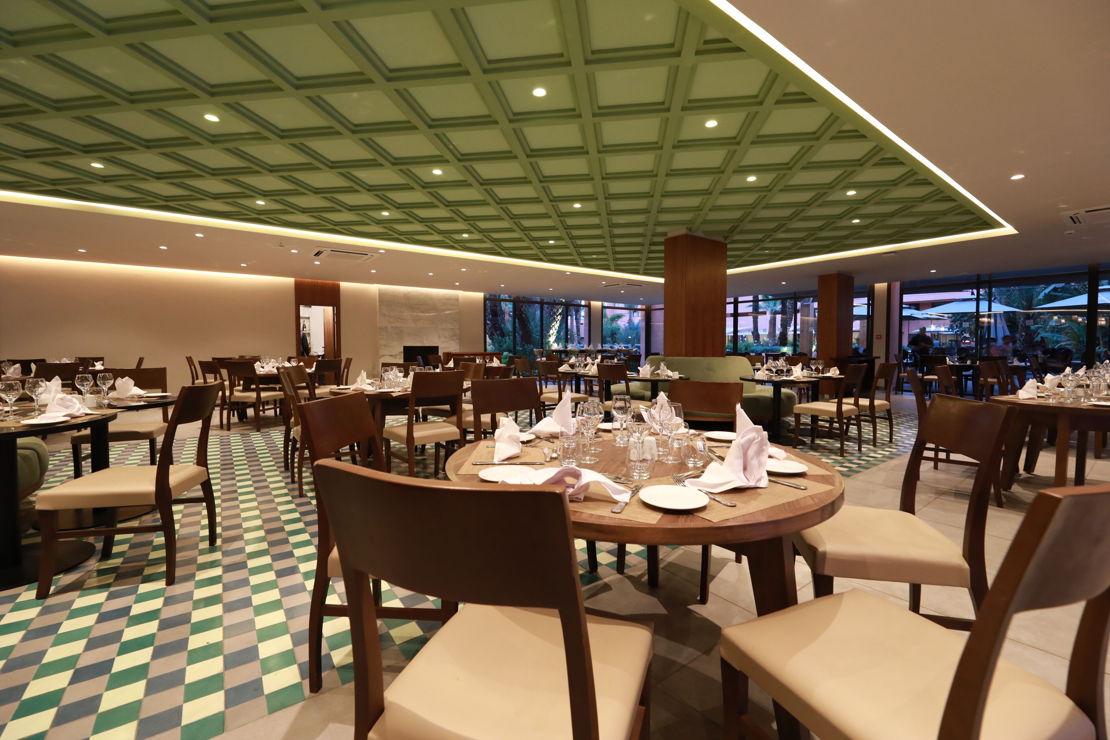 A spacious dining area with round tables, chairs, and a checkered floor pattern.