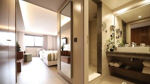 Una habitación de hotel moderna con un espejo grande, un vestidor, un baño con ducha y una cama con vistas a la ciudad.