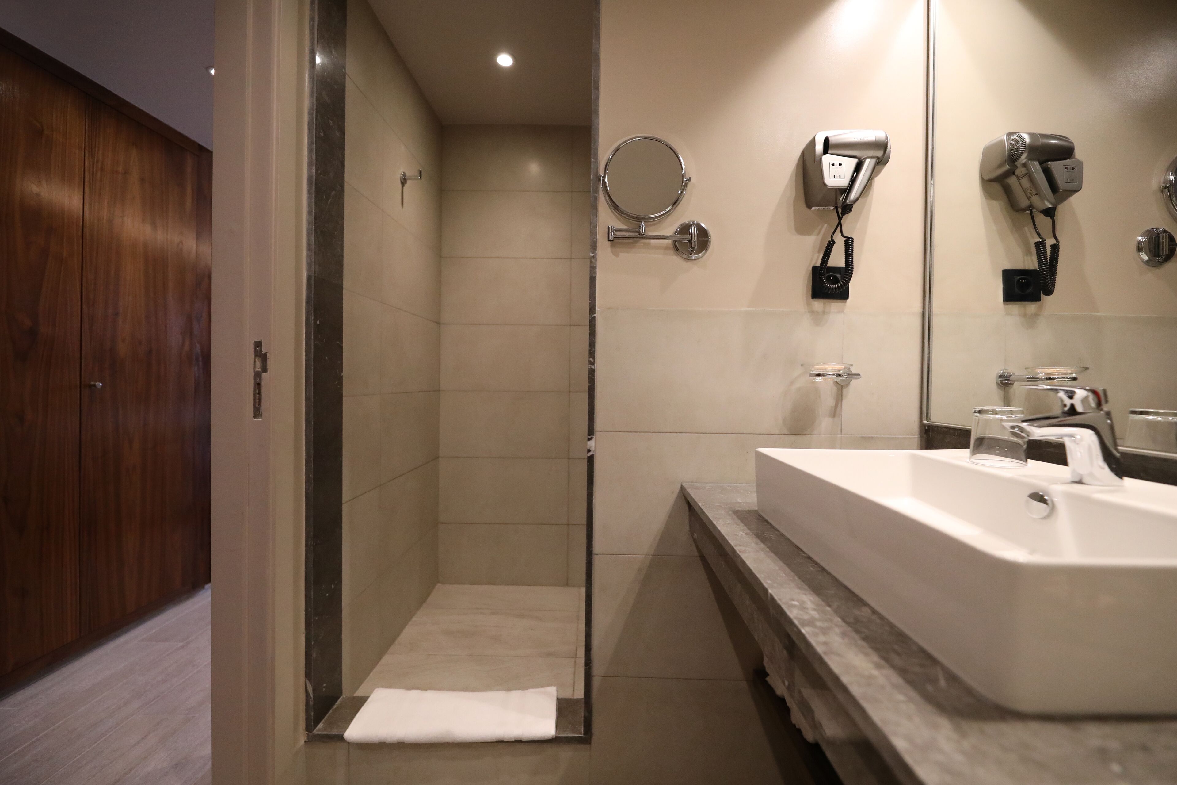 Casa de banho moderna com cabine de duche, lavatório espaçoso e secador de cabelo fixado na parede.
