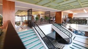 Un moderno vestíbulo de hotel con una escalera central, zonas de estar y un techo decorativo.